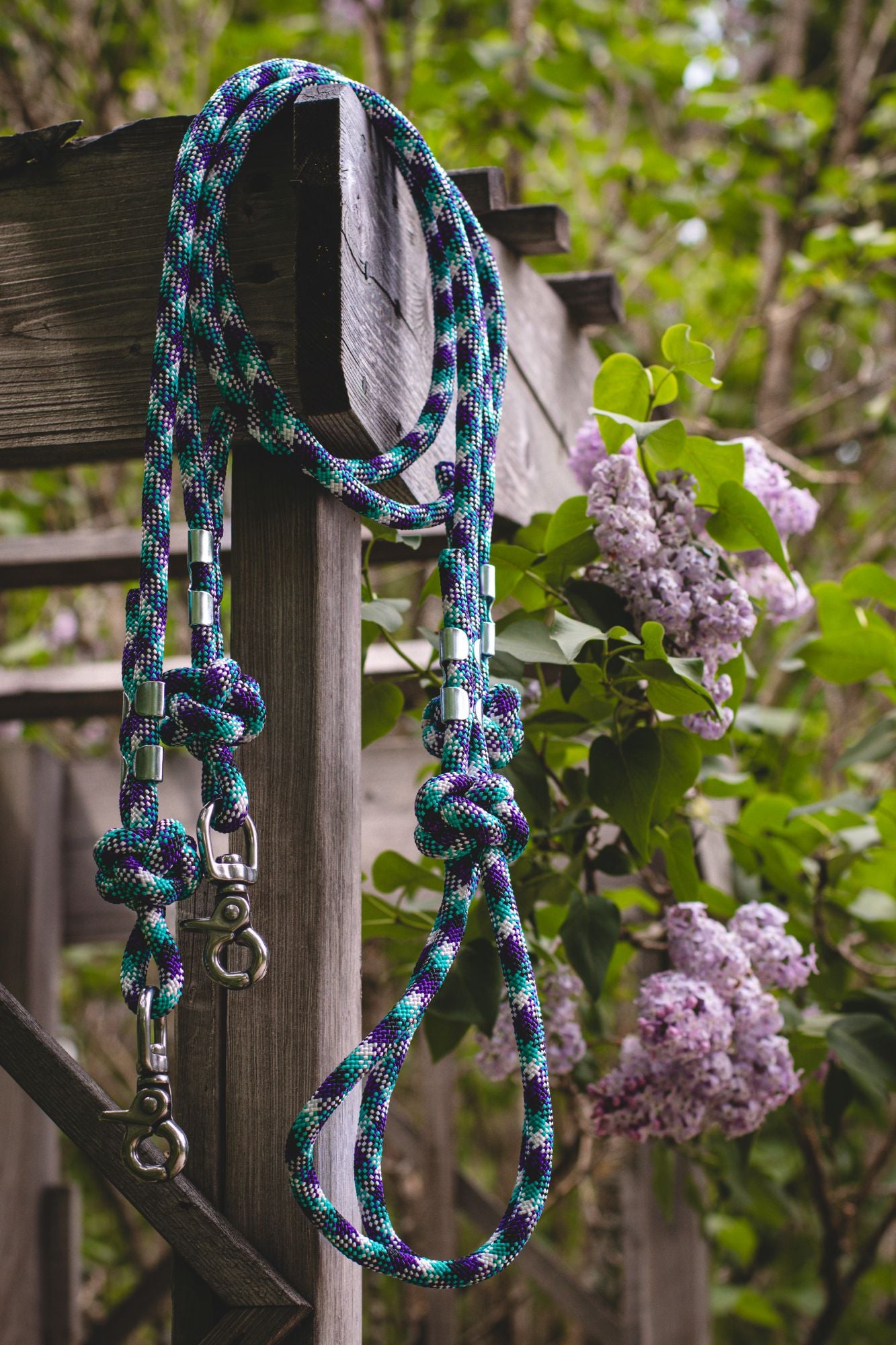 Rope dog leash with knots hanging on a wooden post with greenery in the background