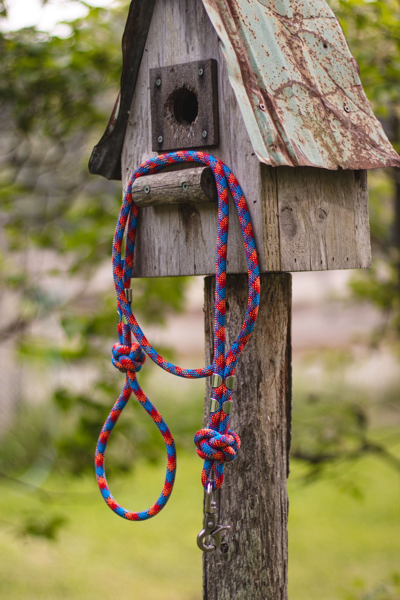 Wooden birdhouse with a colorful rope tied to it, set against a natural background.
