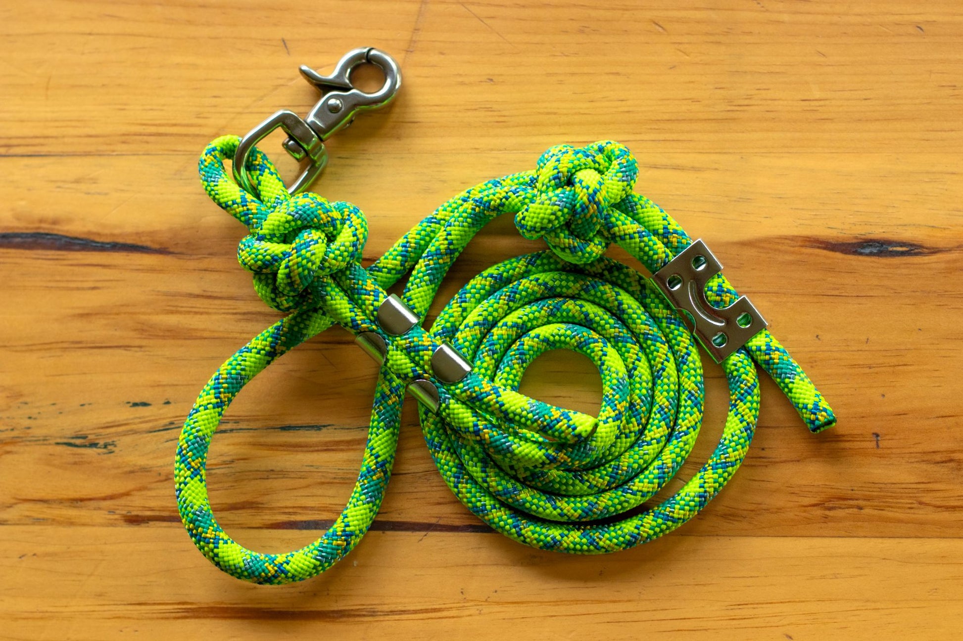 Green and blue rope dog leash with metal clasp on a wooden surface