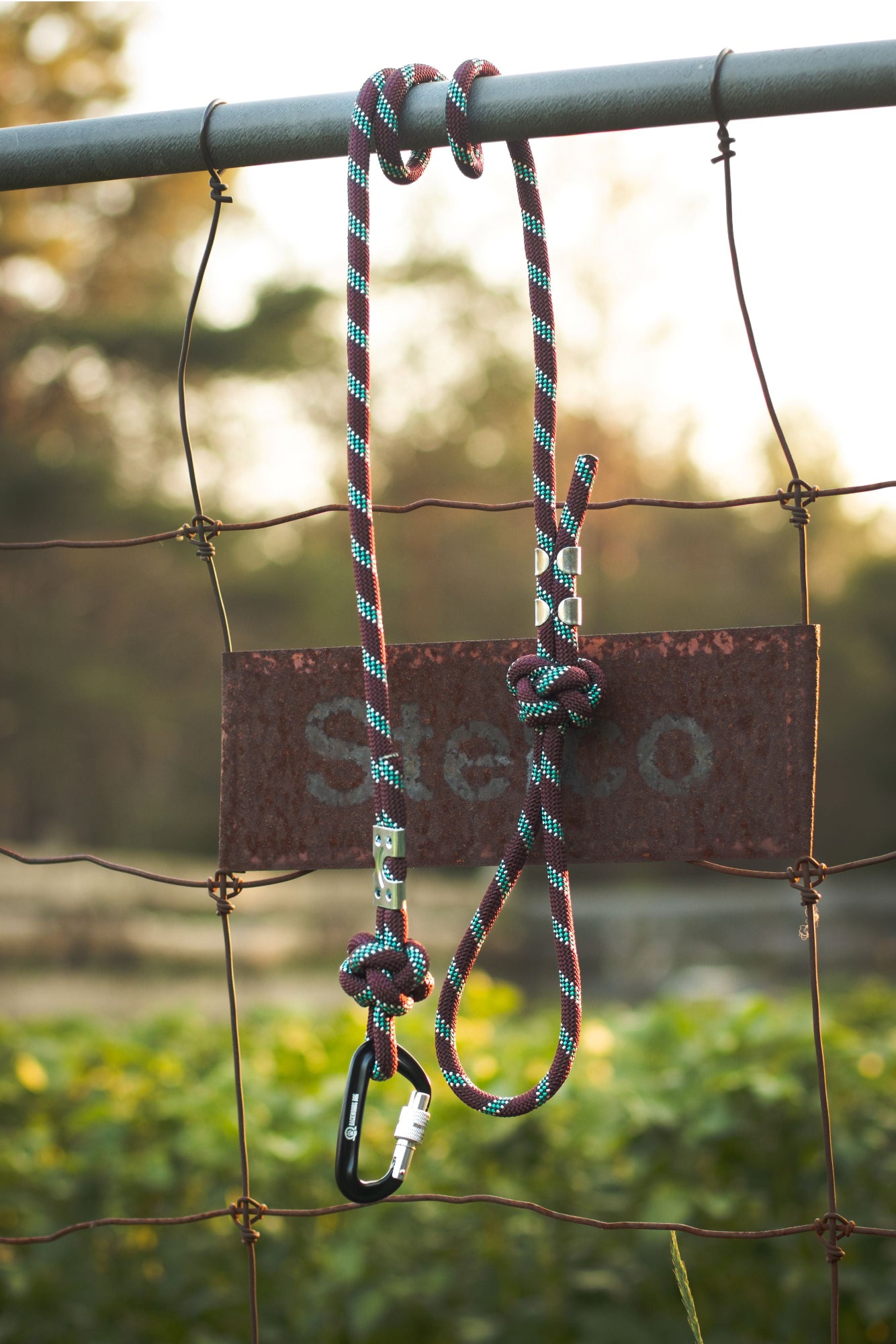 Multicolored rope with carabiner attached to a metal fence, with 'Stecco' branding.