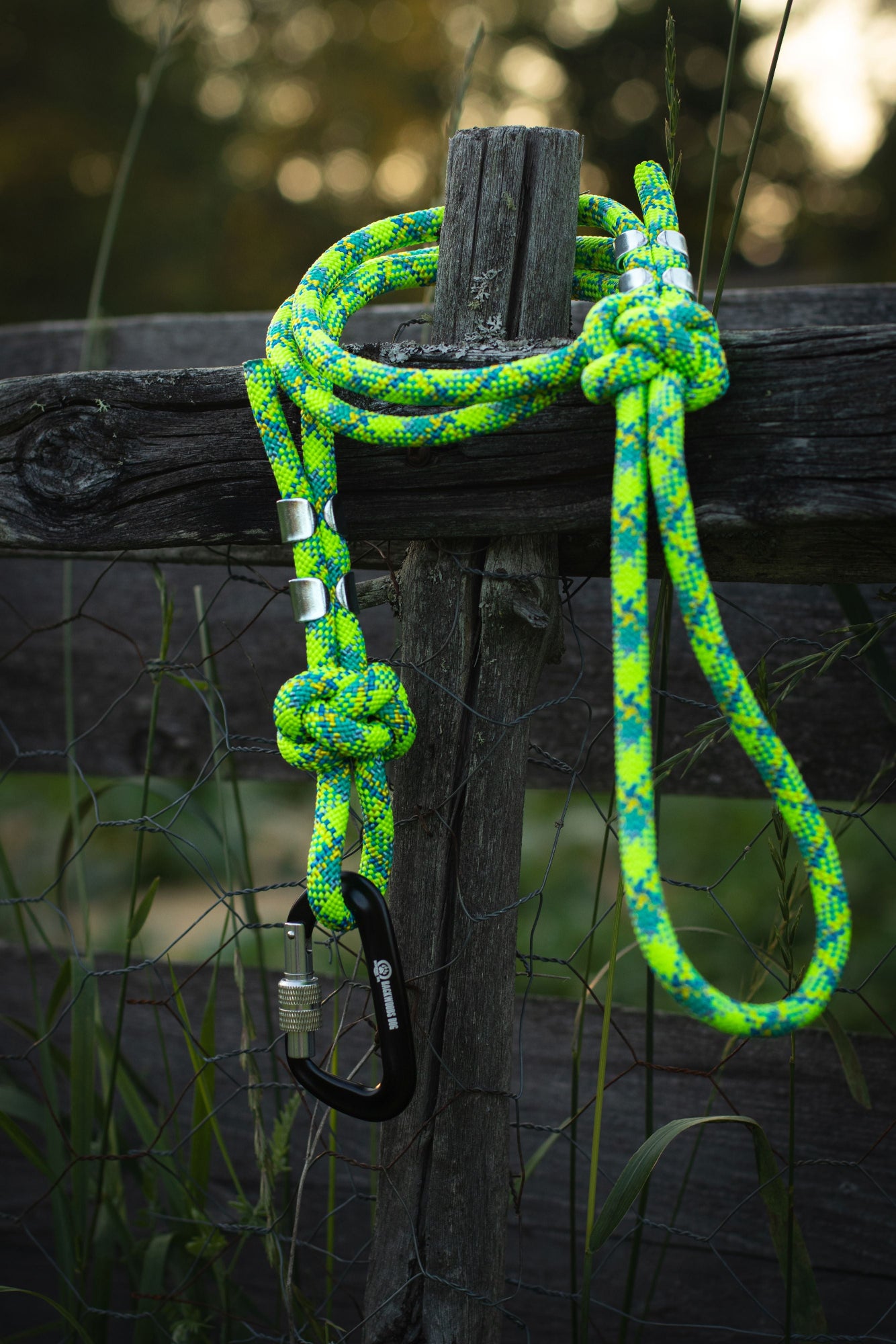 Green and blue rope with a carabiner attached to a wooden post outdoors.
