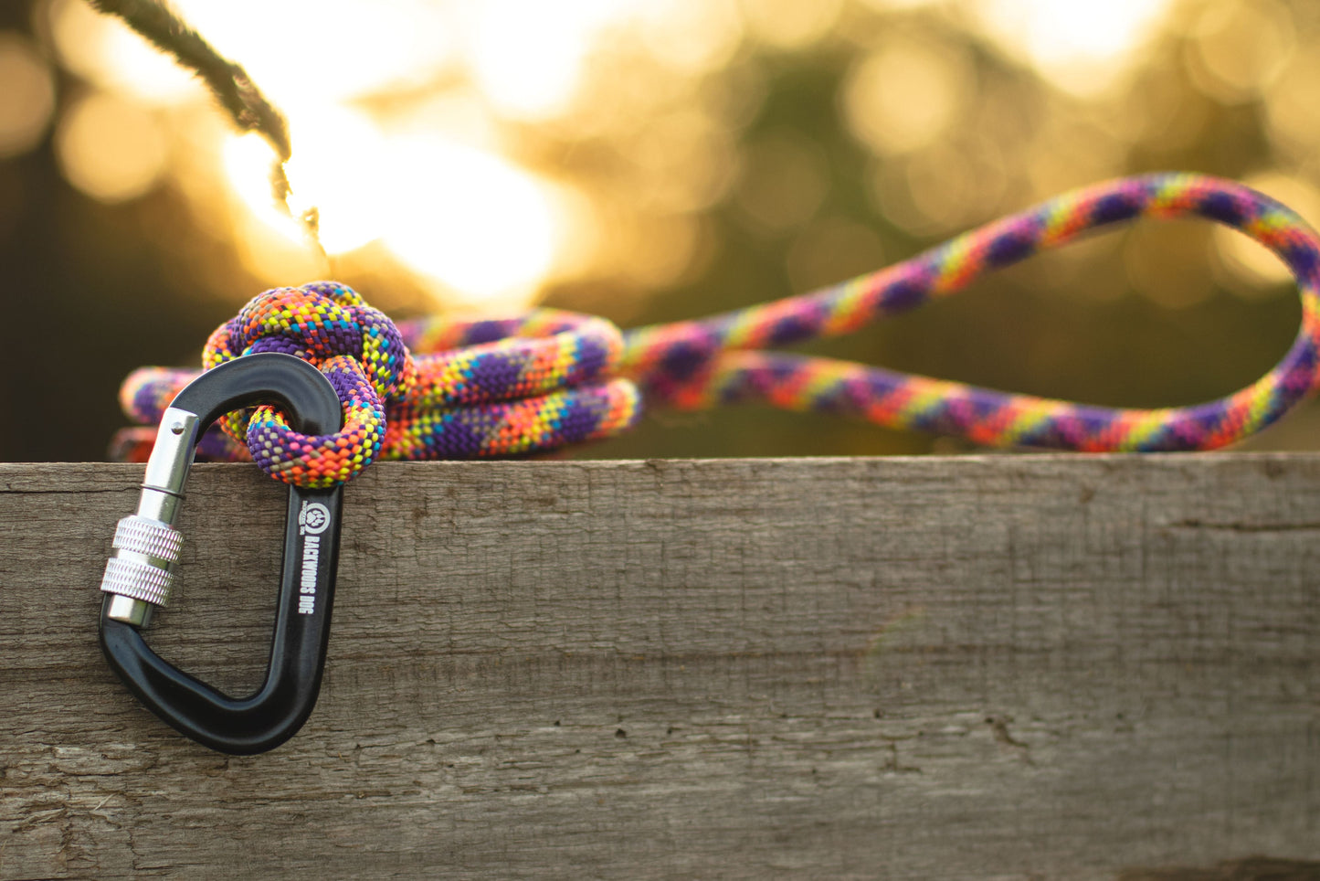 Colorful rope tied to a carabiner on a wooden surface with a blurred natural background